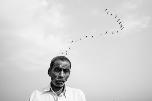 Man in black and white in front of grey sky with birds